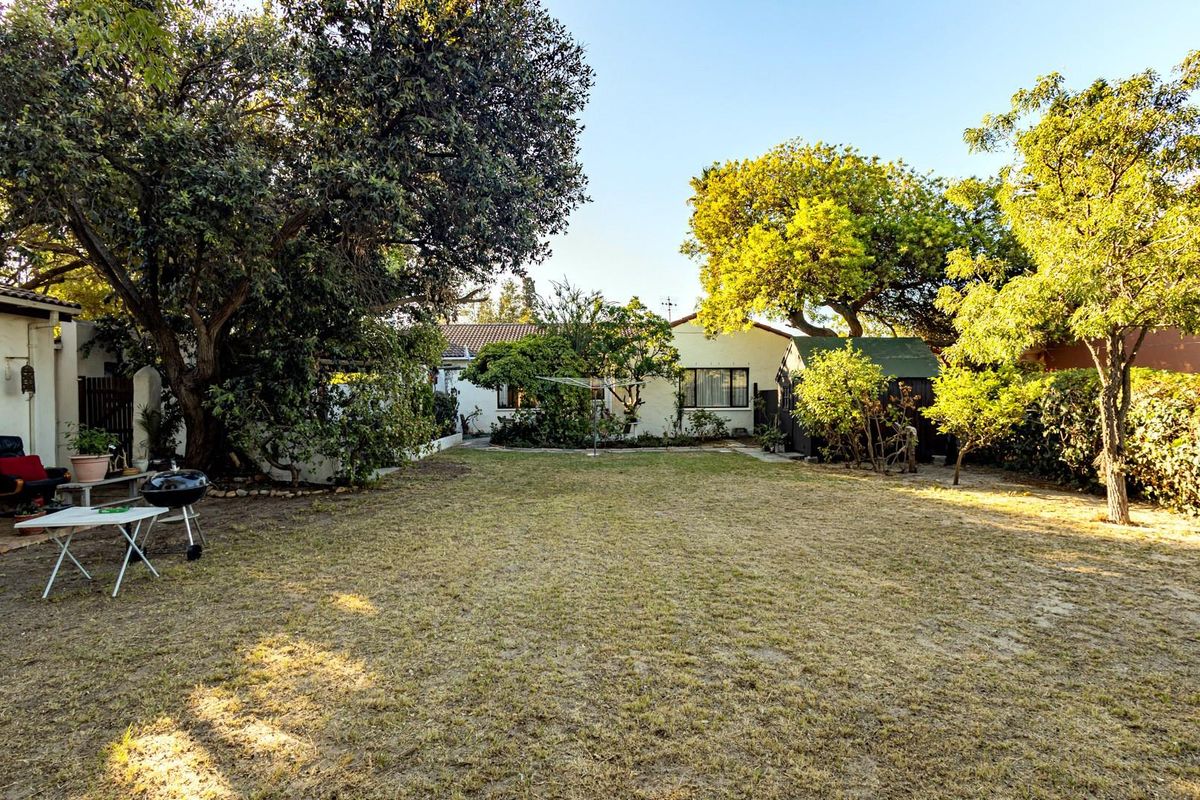 A spacious rear garden featuring mature trees, a lawn area, and a small storage shed, providing a private outdoor space.