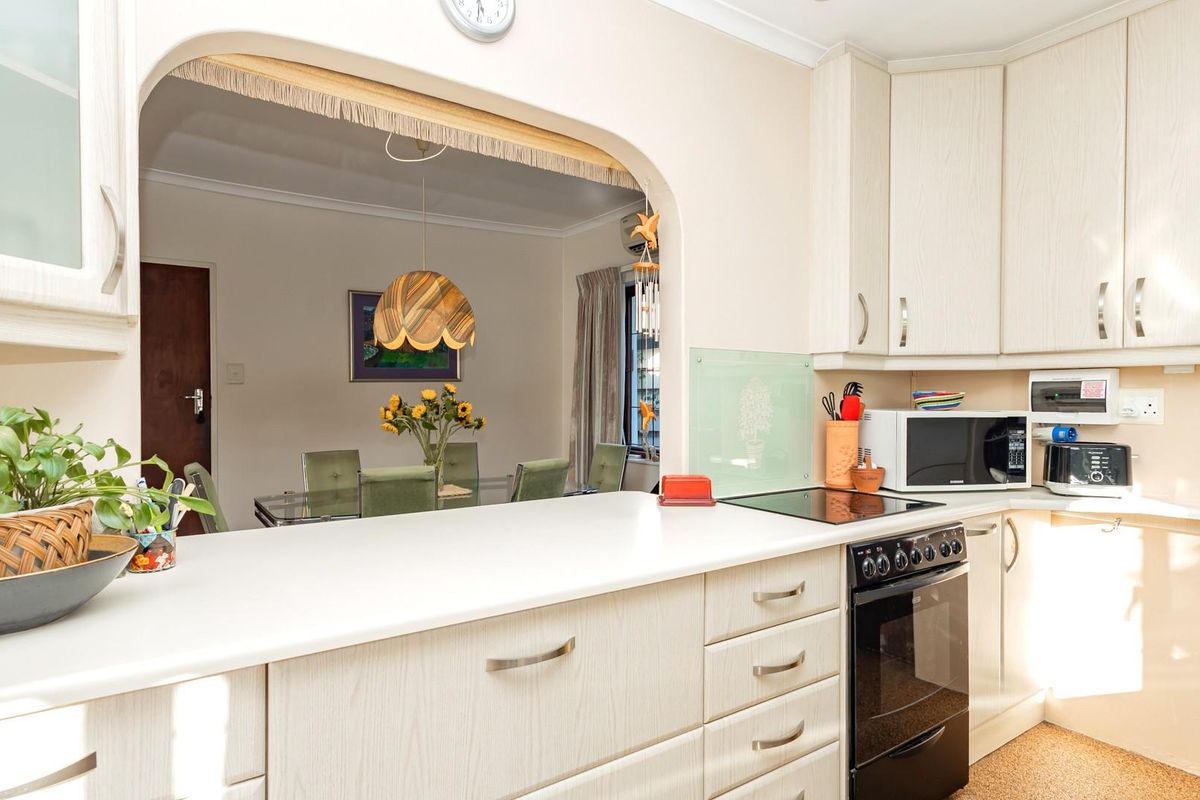 A functional kitchen featuring light wood-grain cabinetry, a built-in oven with a glass cooktop, and a convenient serving hatch opening into the dining area.