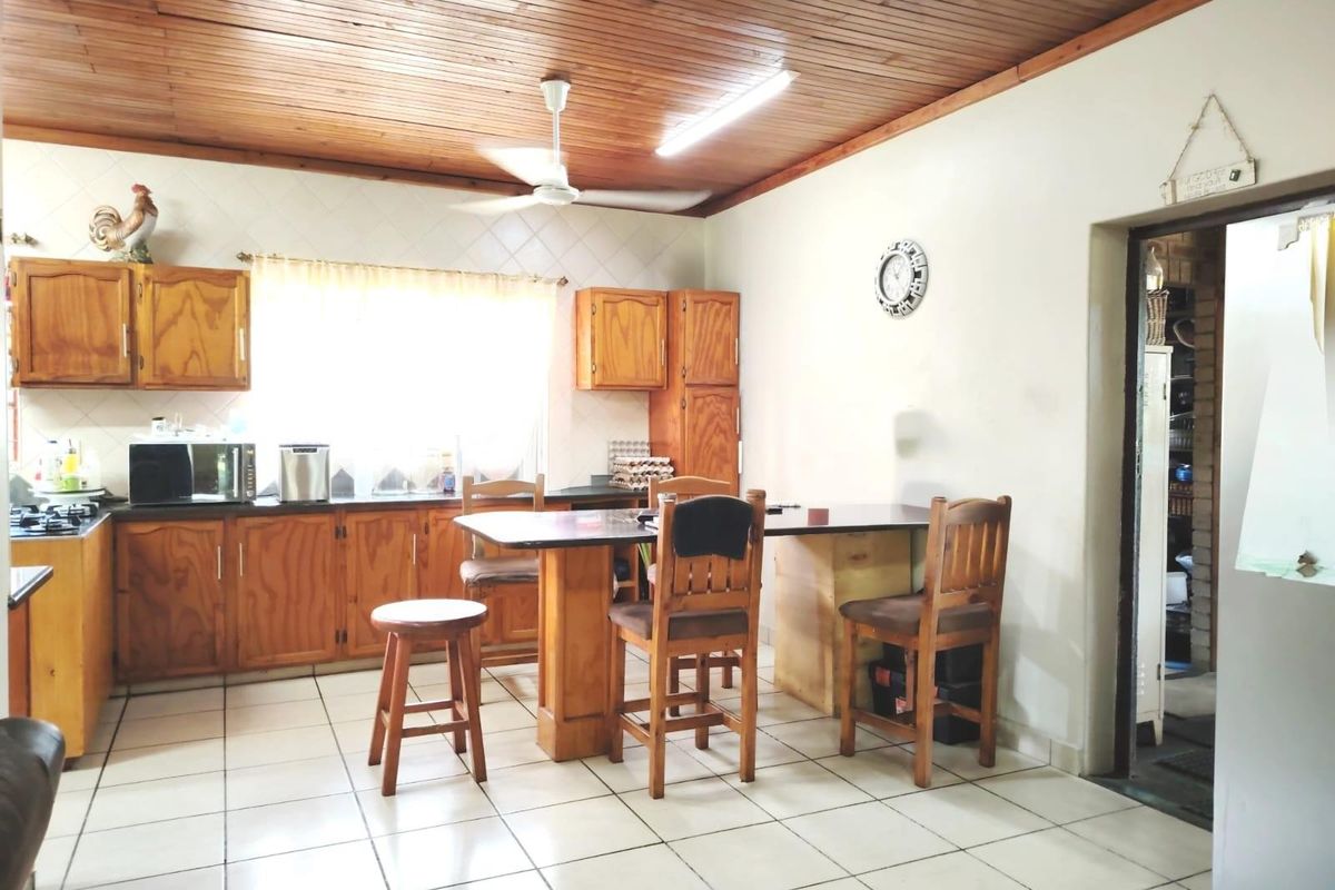 A functional kitchen featuring wooden cabinetry, tiled flooring, and a timber-clad ceiling with an integrated breakfast bar area.