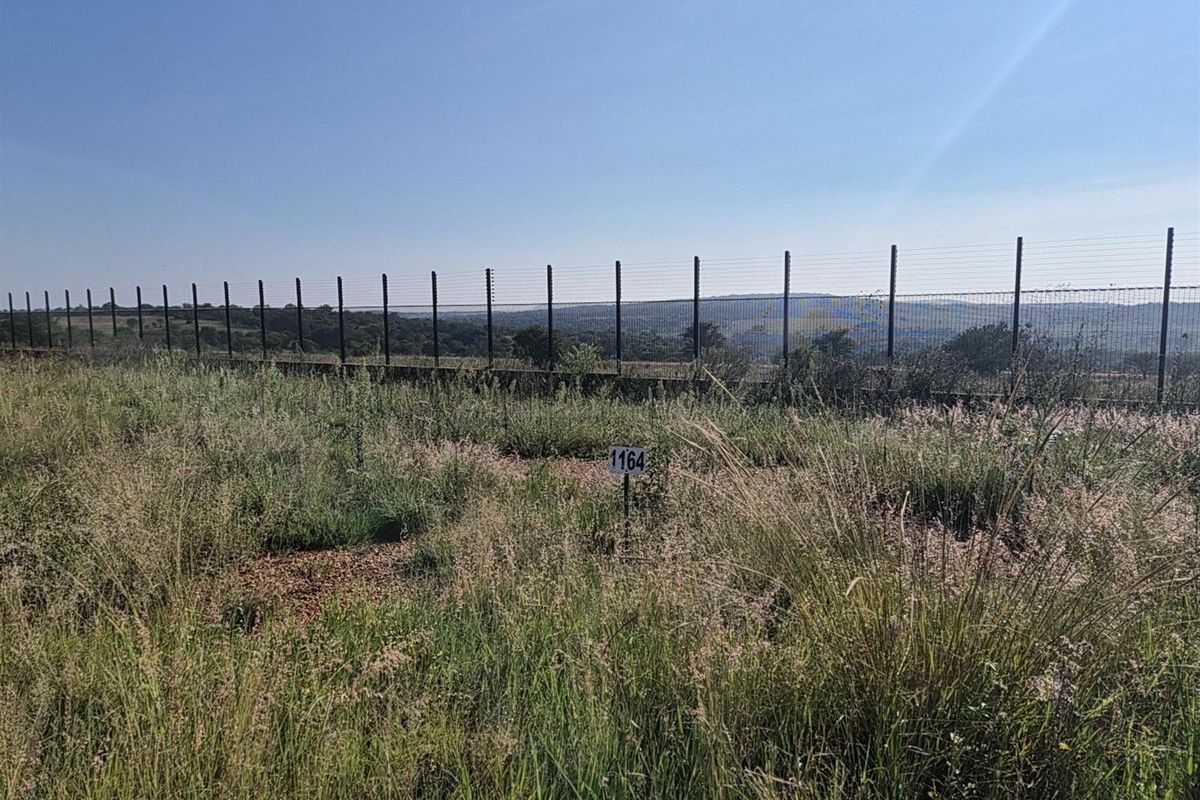 A vacant residential plot featuring natural grass coverage, enclosed by a perimeter fence with an elevated view of the surrounding landscape.