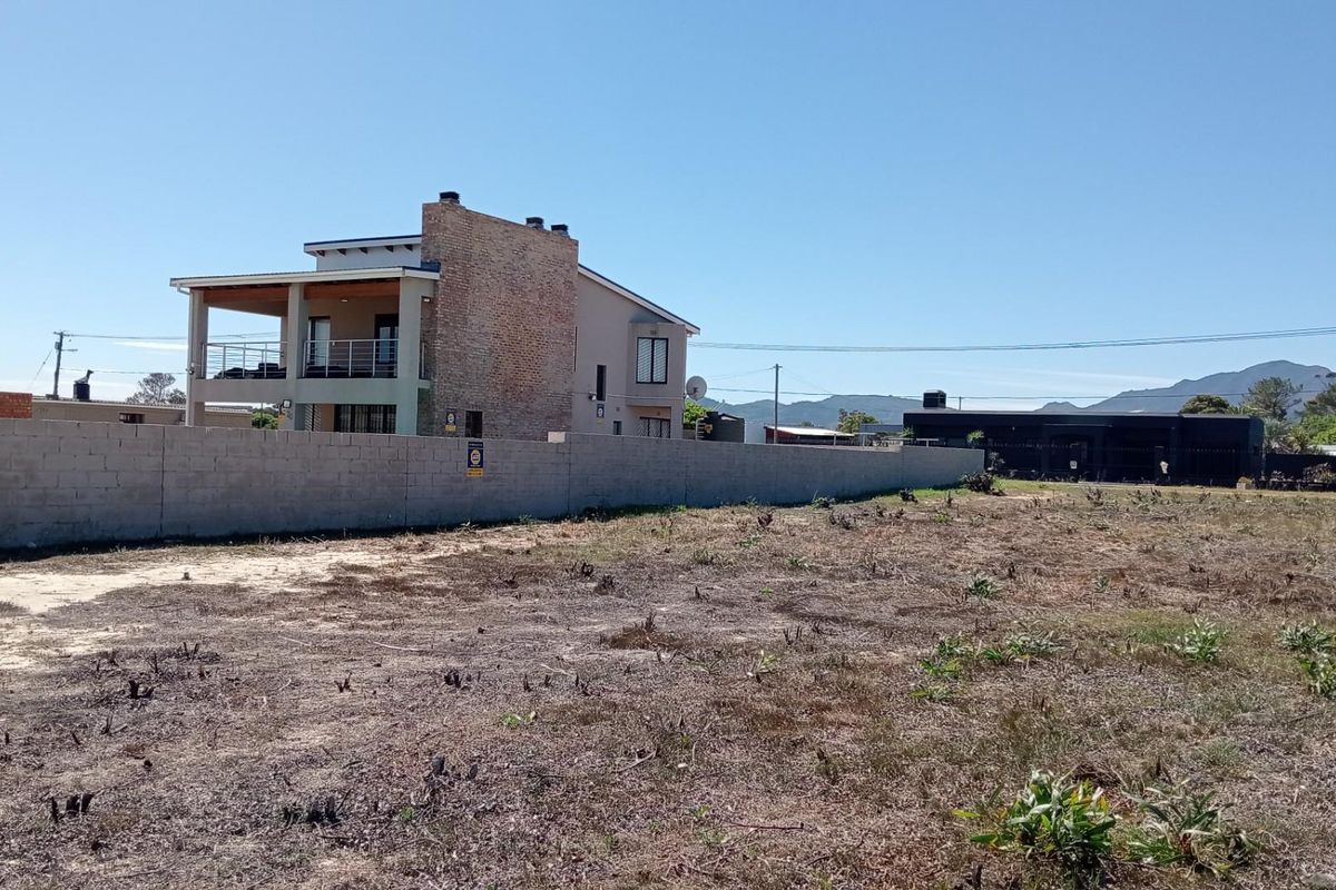 A view of a vacant residential plot of land enclosed by a perimeter boundary wall, with neighboring properties visible in the background.