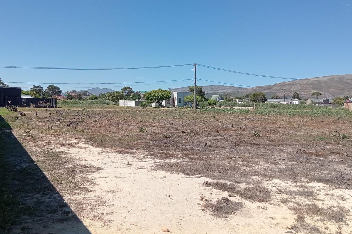 A vacant residential plot featuring a boundary wall and views of the surrounding neighborhood and distant mountains.