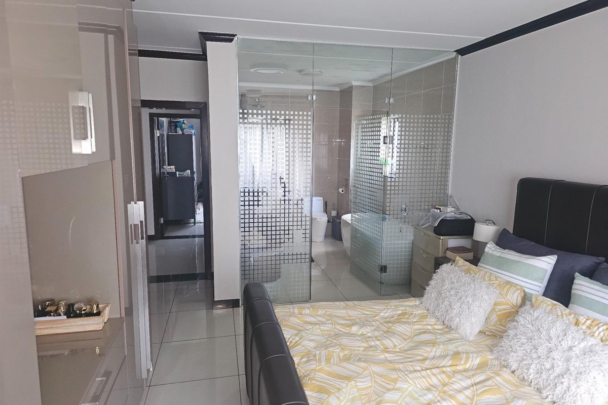 Modern bedroom featuring tiled flooring, built-in cupboards, and a contemporary glass-enclosed en-suite bathroom.