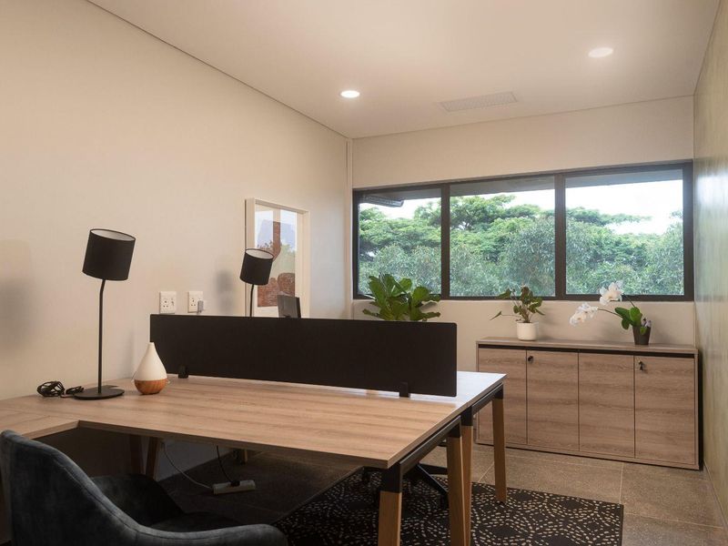 A modern, well-lit office space featuring built-in cabinetry, large windows with garden views, and high-quality tiled flooring.