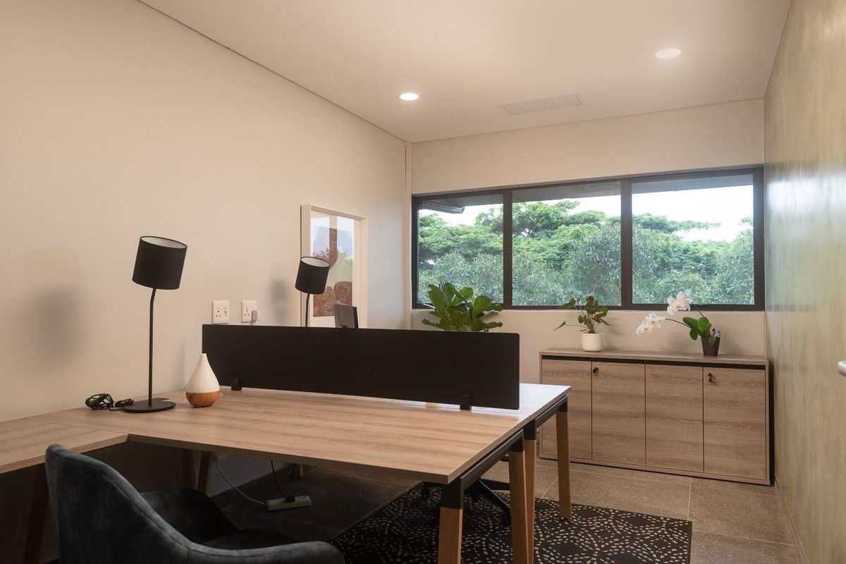 A modern, well-lit office space featuring built-in cabinetry, large windows with garden views, and high-quality tiled flooring.