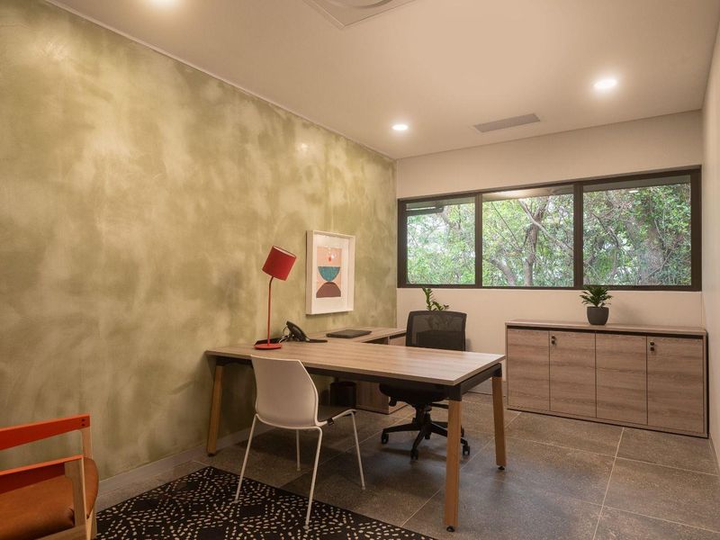 A modern, well-lit office space featuring tiled flooring, built-in cabinetry, and a large window providing natural light and a pleasant outdoor view.