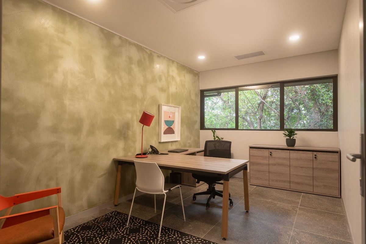 A modern, well-lit office space featuring tiled flooring, built-in cabinetry, and a large window providing natural light and a pleasant outdoor view.