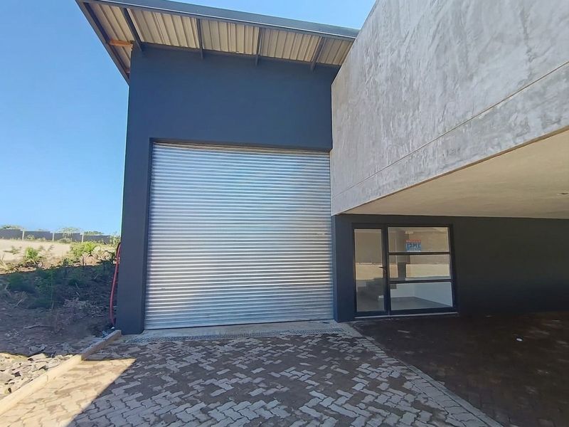 Modern industrial facade featuring a large metal roller shutter door, glass entrance, and paved driveway area.