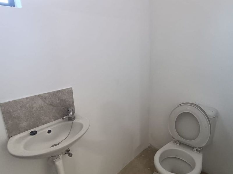A basic industrial-style bathroom featuring a wall-mounted basin and toilet, currently in a shell-like condition with unfinished flooring.