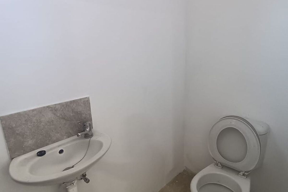 A basic industrial-style bathroom featuring a wall-mounted basin and toilet, currently in a shell-like condition with unfinished flooring.