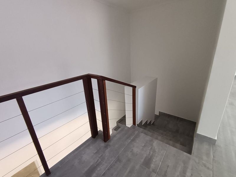 A clean, modern staircase featuring dark grey tiled steps, a timber handrail, and a minimalist wire balustrade system.