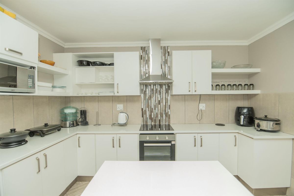 Modern kitchen featuring white cabinetry, stone countertops, a tiled backsplash, and integrated stainless steel appliances including an oven and extractor fan.