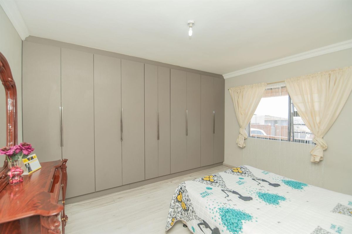 A well-maintained bedroom featuring extensive floor-to-ceiling built-in cupboards, light-toned laminate flooring, and neutral wall finishes.