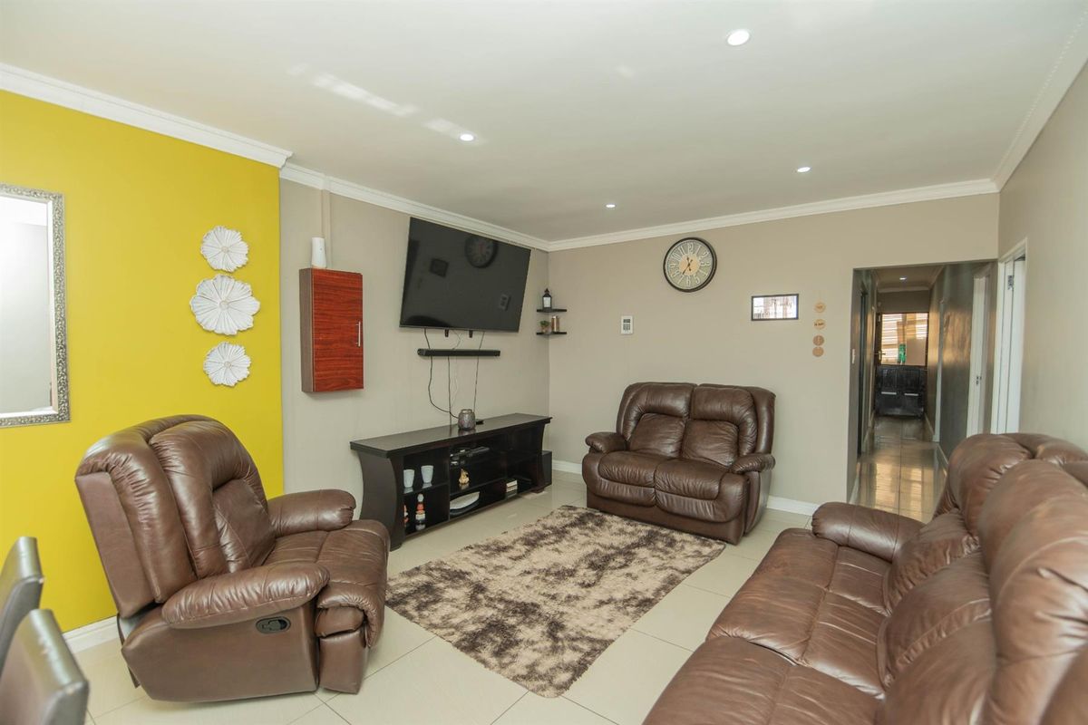 A comfortable living room featuring tiled flooring, recessed downlighting, and a vibrant yellow accent wall, providing a functional and well-maintained space.