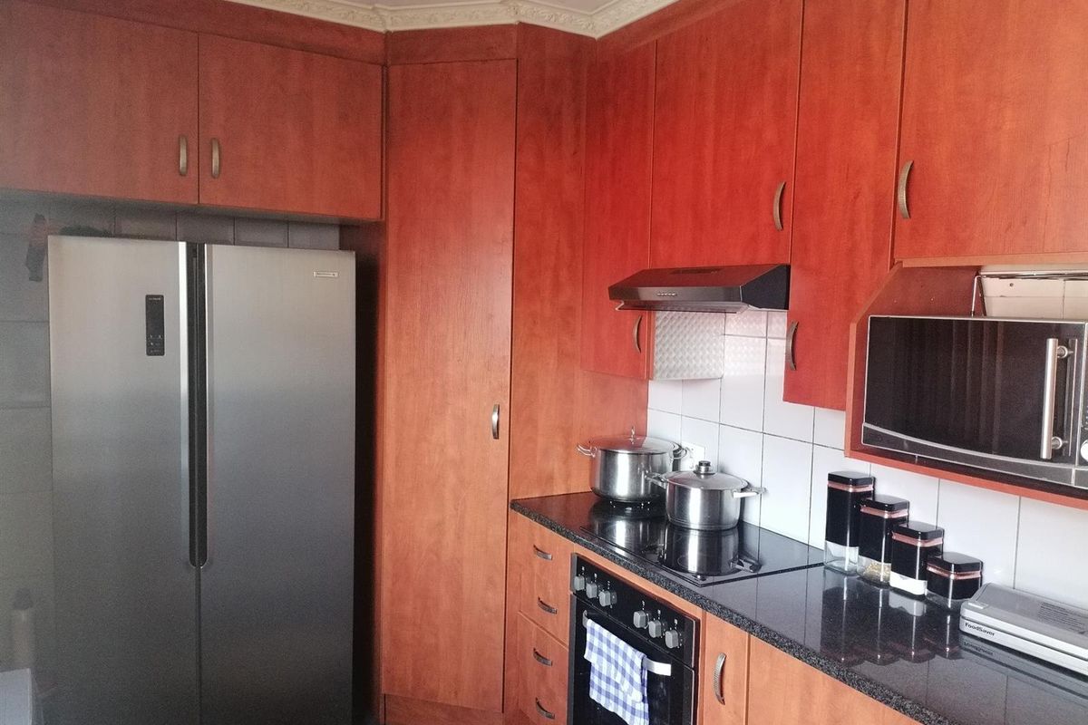 A functional kitchen featuring warm-toned wooden cabinetry, dark granite countertops, a built-in oven, hob, and extractor fan with tiled splashbacks.
