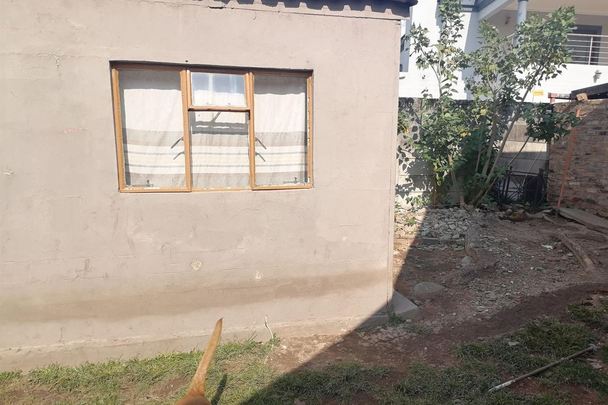 Exterior view of a detached utility structure featuring a basic window and weathered plaster finish, situated in a rear garden area.