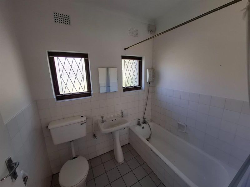 A dated bathroom featuring a pedestal basin, toilet, and bathtub with tiled finishes and leaded glass windows, offering potential for modernization.