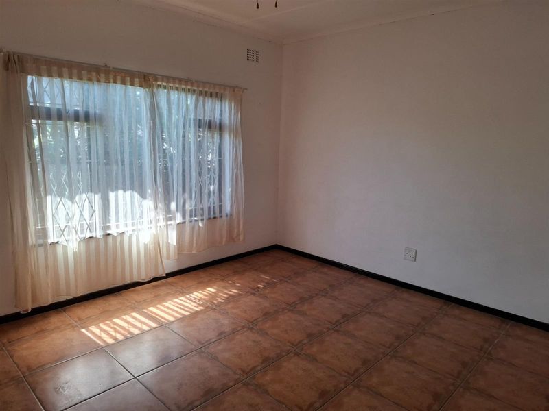 An empty bedroom featuring tiled flooring, a large window with a security gate, and neutral wall finishes.