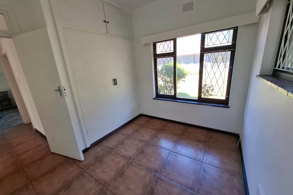 An empty bedroom featuring tiled flooring, built-in cupboards, and leaded glass windows with security bars, offering a blank canvas for personalization.