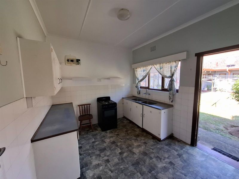 Functional kitchen featuring built-in cabinetry, double sink, and freestanding stove, with direct access to the rear garden area.