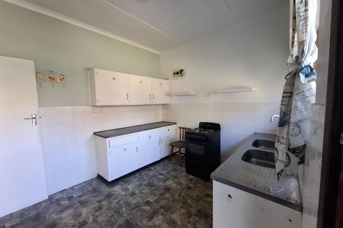 A functional kitchen featuring built-in cabinetry, a double sink, and a tiled splashback, offering a blank canvas for potential modern updates.