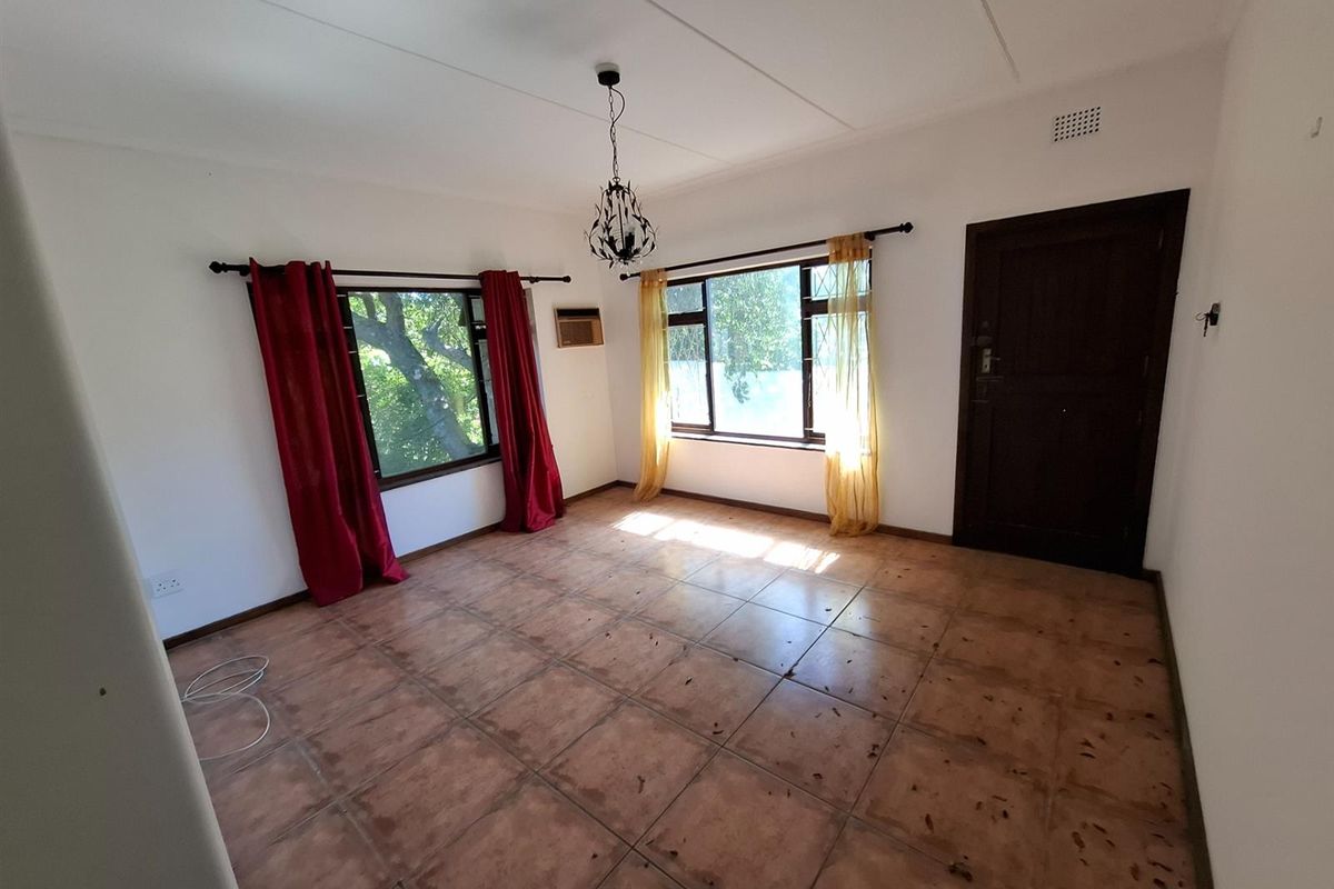 An empty living room featuring tiled flooring, an air conditioning unit, and large windows with security bars, offering a blank canvas for interior design.