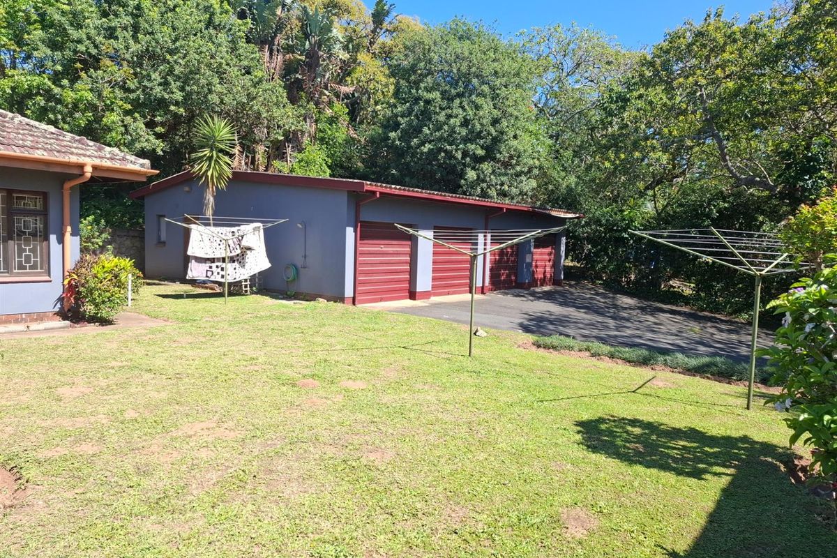 Rear view of the property featuring a triple garage with red roller doors, a paved driveway, and a spacious lawn area.