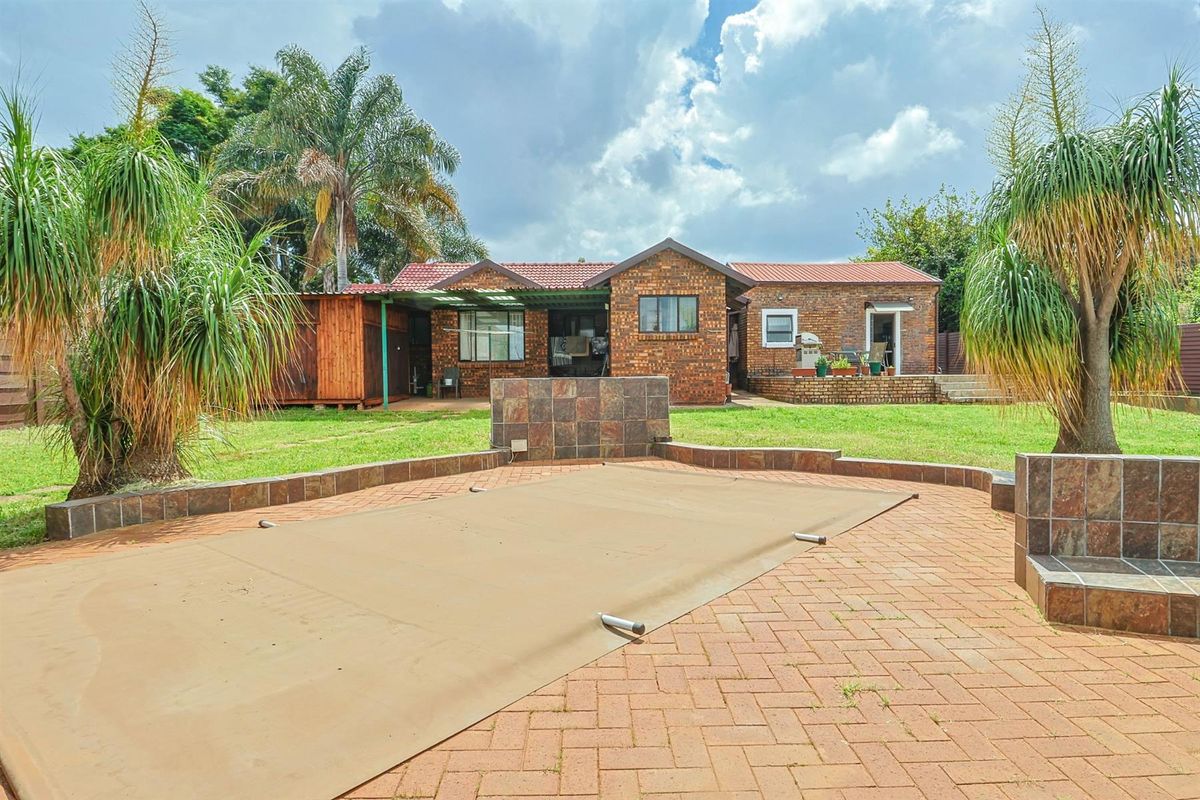 Rear view of the property featuring a brick facade, a paved pool area with a cover, and a spacious garden.
