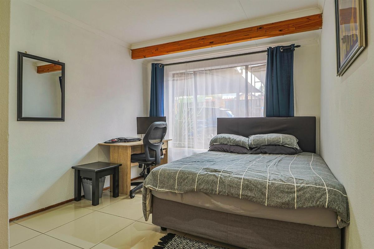 A functional bedroom featuring tiled flooring, a large window with natural light, and exposed timber ceiling beams.