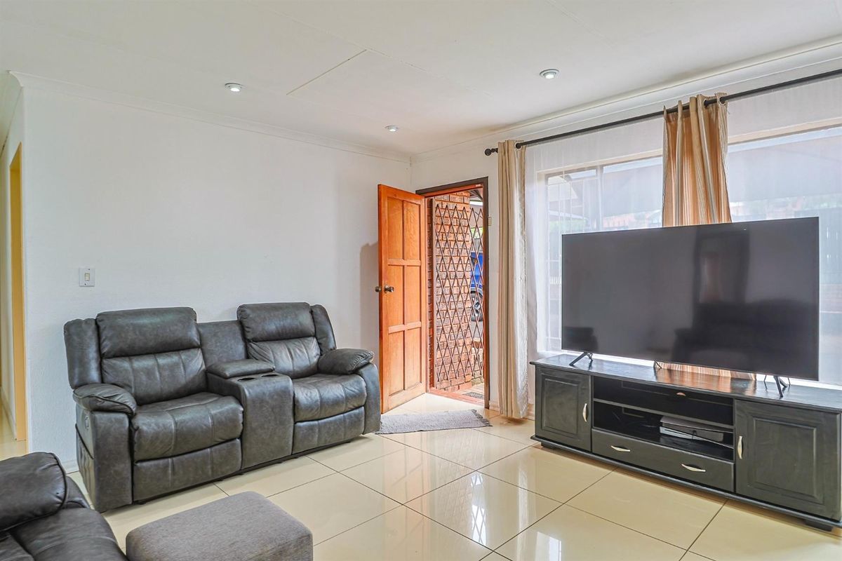 A bright living room featuring polished porcelain floor tiles, recessed downlighting, and direct access to the exterior through a wooden door.