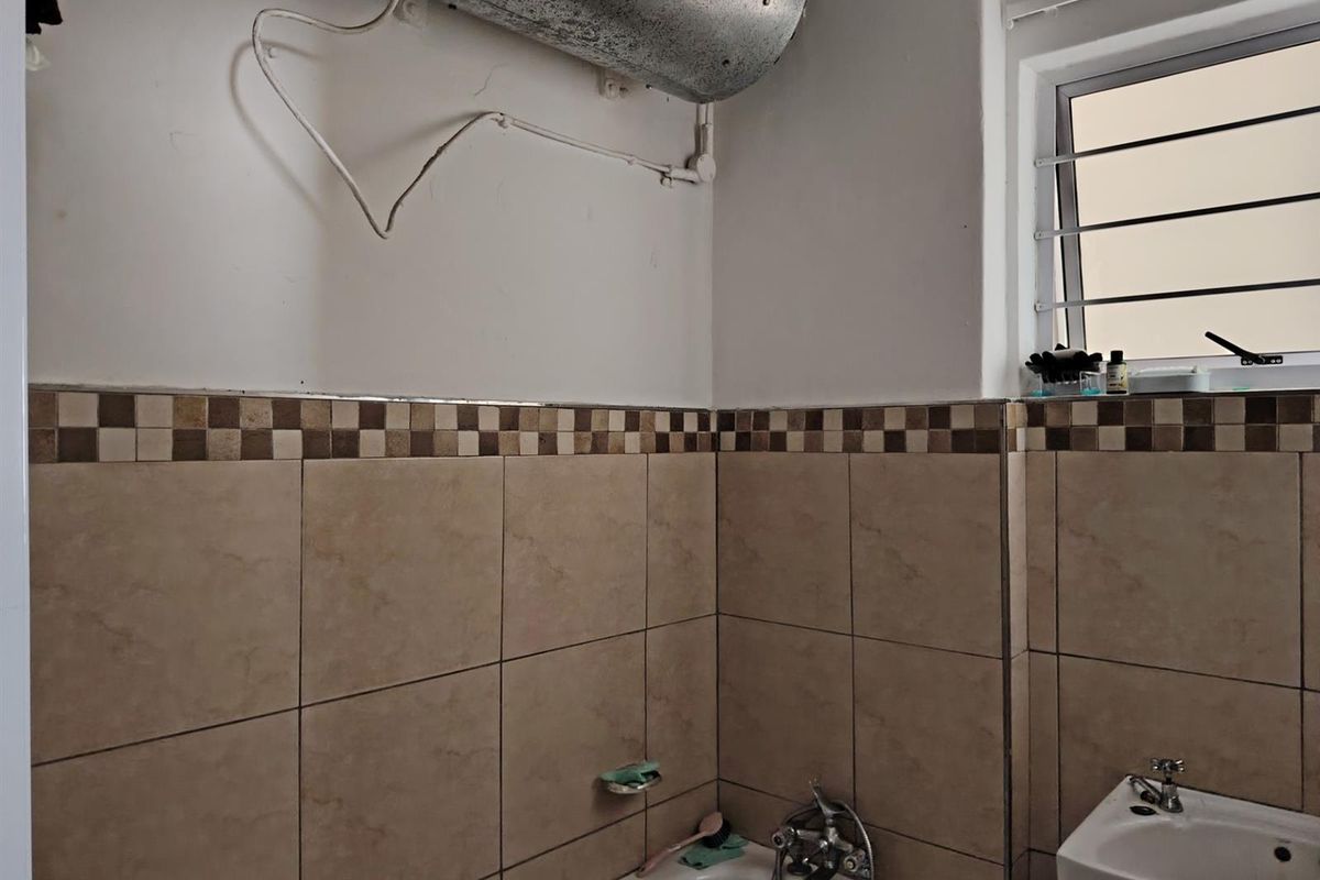 A dated bathroom featuring tiled walls, a bathtub with mixer tap, a wall-mounted basin, and exposed ventilation ducting.