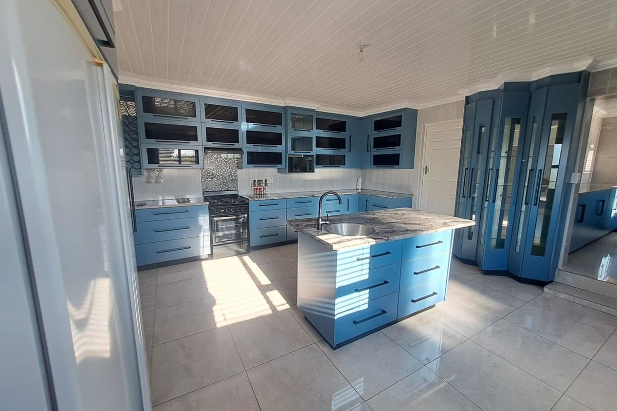 Modern kitchen featuring blue cabinetry, a central island with stone countertops, tiled flooring, and a distinctive tongue and groove ceiling.