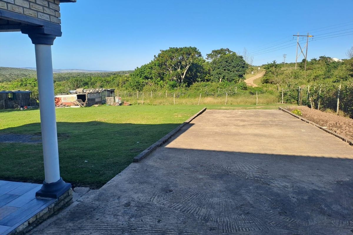 Spacious rear yard featuring a large concrete driveway, expansive lawn, and perimeter fencing with scenic rural views.