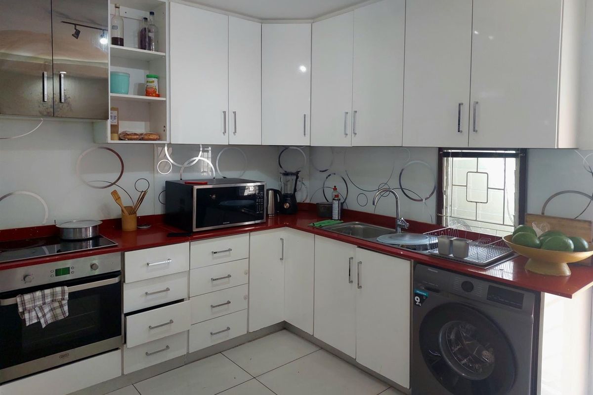 Modern kitchen featuring white cabinetry, contrasting red countertops, integrated oven, hob, extractor fan, and a built-in space for a washing machine.