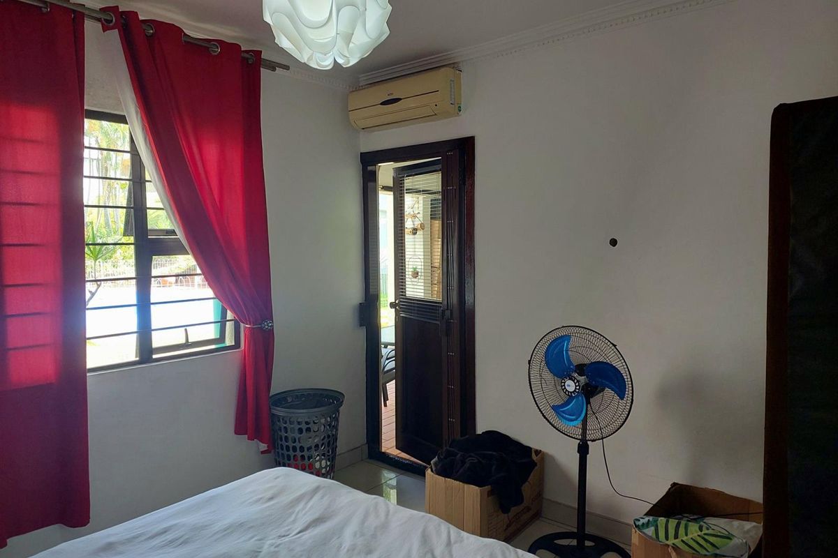 A bedroom featuring a window with security bars, a wall-mounted air conditioning unit, and a door providing access to an outdoor area.