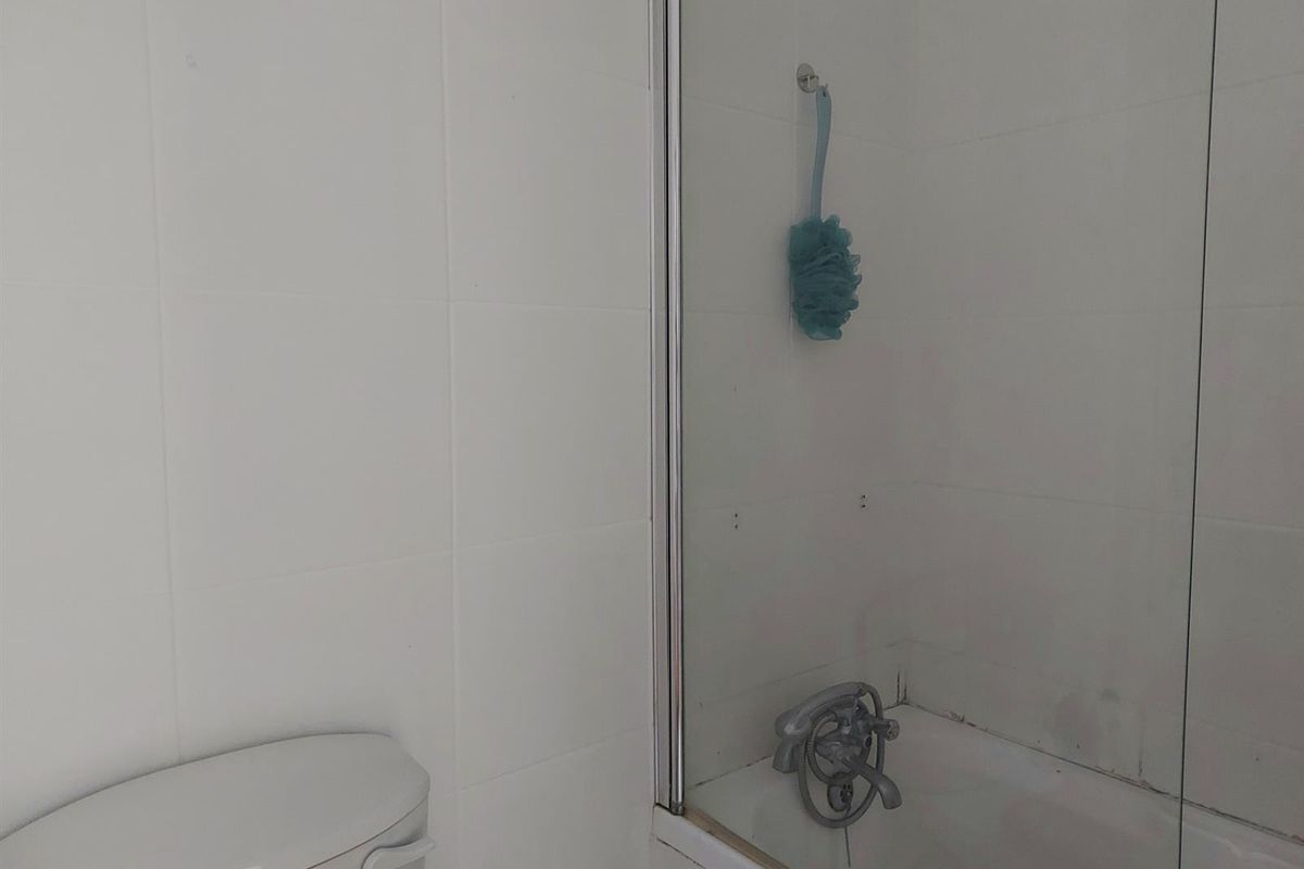 A functional bathroom featuring a white bathtub with a glass shower screen and a standard toilet.