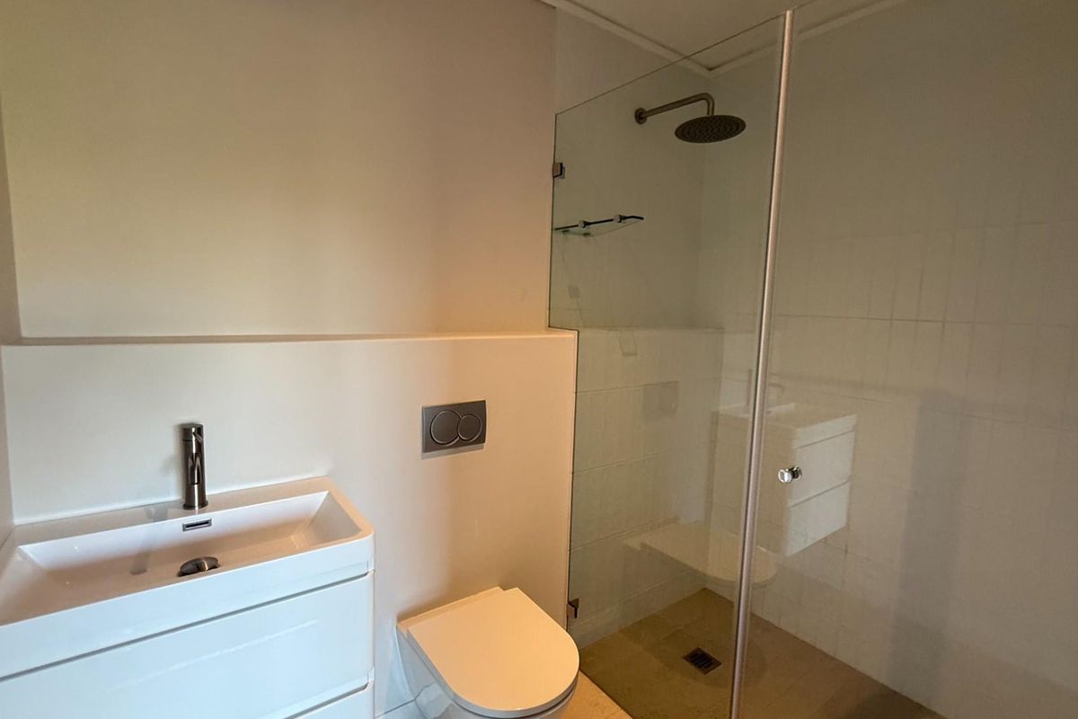 Modern bathroom featuring a wall-mounted vanity, concealed cistern toilet, and a walk-in shower with a glass partition and rainfall showerhead.