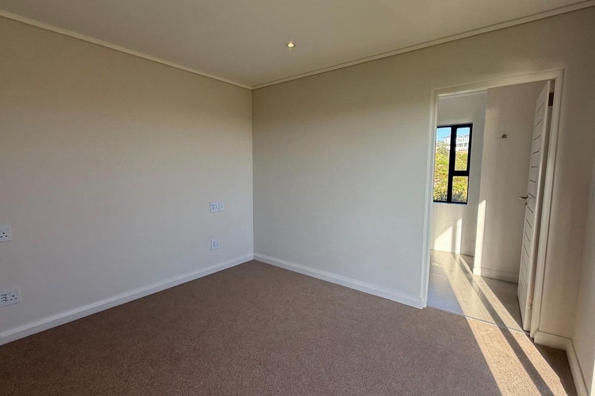 A clean, empty bedroom featuring neutral carpeting, recessed ceiling lighting, and a doorway leading to an adjacent tiled space.
