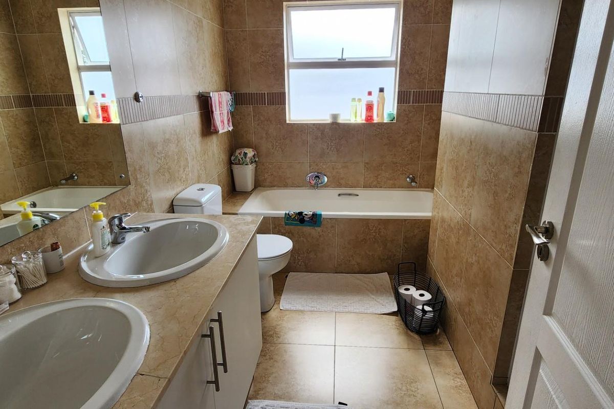 A functional bathroom featuring a double vanity with integrated sinks, a built-in bathtub, and full-height wall tiling.