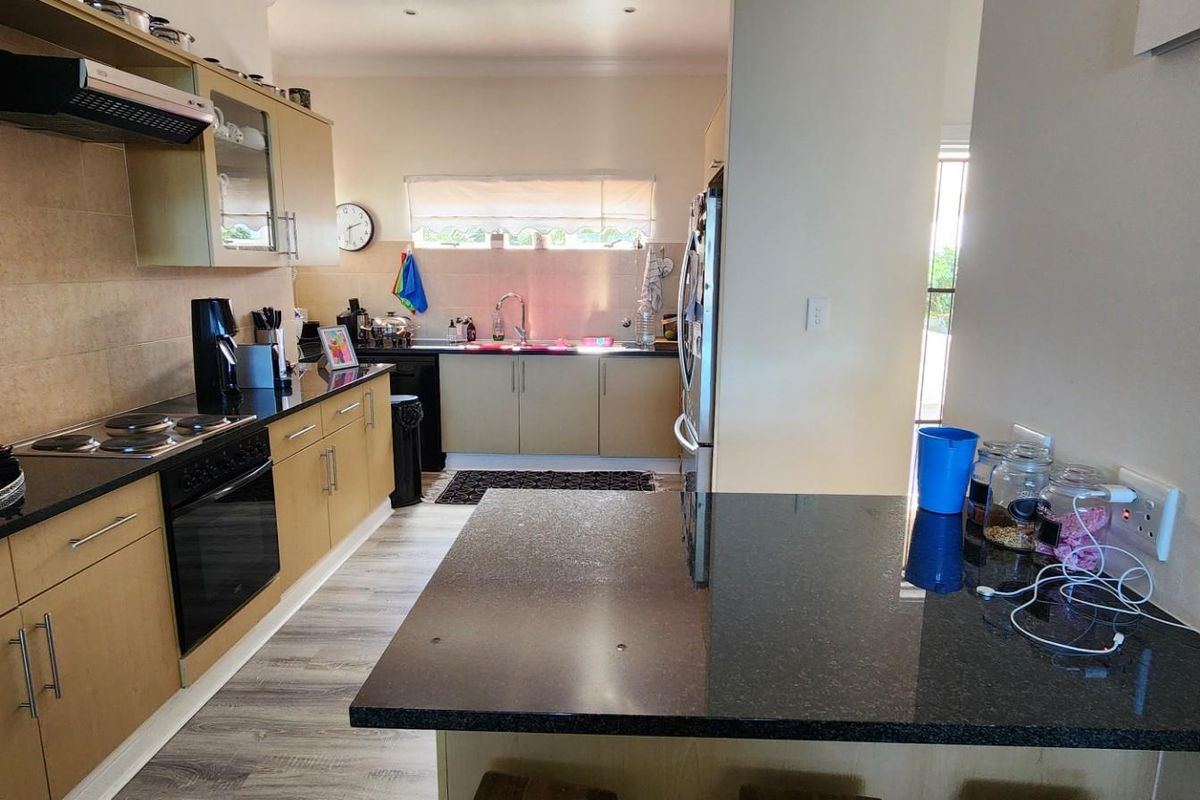 A functional kitchen featuring light wood cabinetry, dark granite countertops, a built-in oven, and a breakfast bar area.