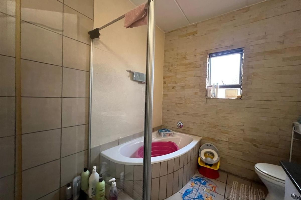 Bathroom featuring a built-in bathtub with a glass shower screen, tiled wall finishes, and a stone-look feature wall.