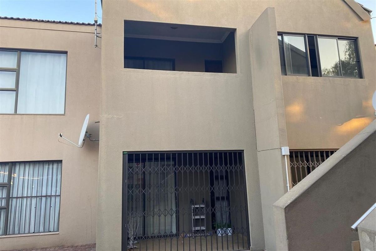 Rear view of the apartment building featuring a ground floor patio with security gate, an upper-level balcony, and exterior plaster finish.