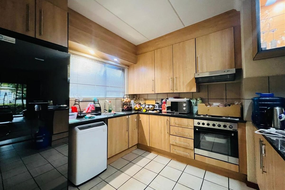 A functional kitchen featuring light wood-finish cabinetry, dark granite countertops, built-in oven, extractor fan, and tiled flooring.