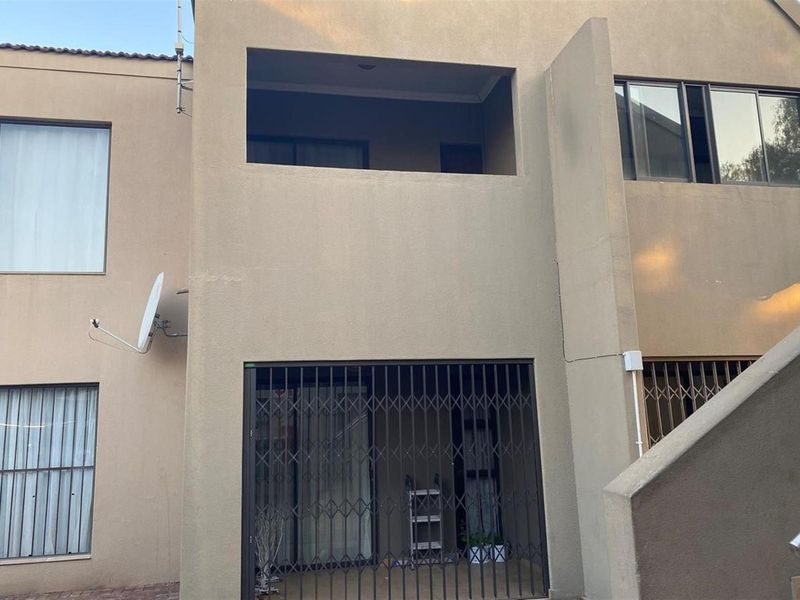 Rear view of the apartment building featuring a ground floor patio with security gate, an upper-level balcony, and exterior plaster finish.