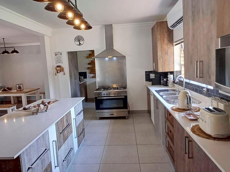 Modern open-plan kitchen featuring a central island, stainless steel gas stove, extractor fan, and sleek cabinetry, seamlessly flowing into the adjacent dining area.