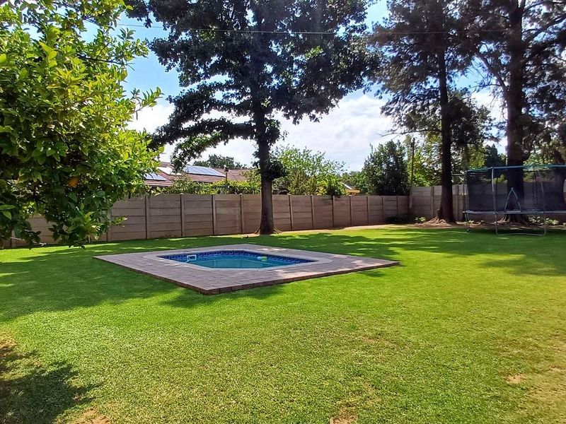 A spacious backyard featuring a well-maintained lawn, a central swimming pool with paved surround, and secure precast concrete boundary walls.
