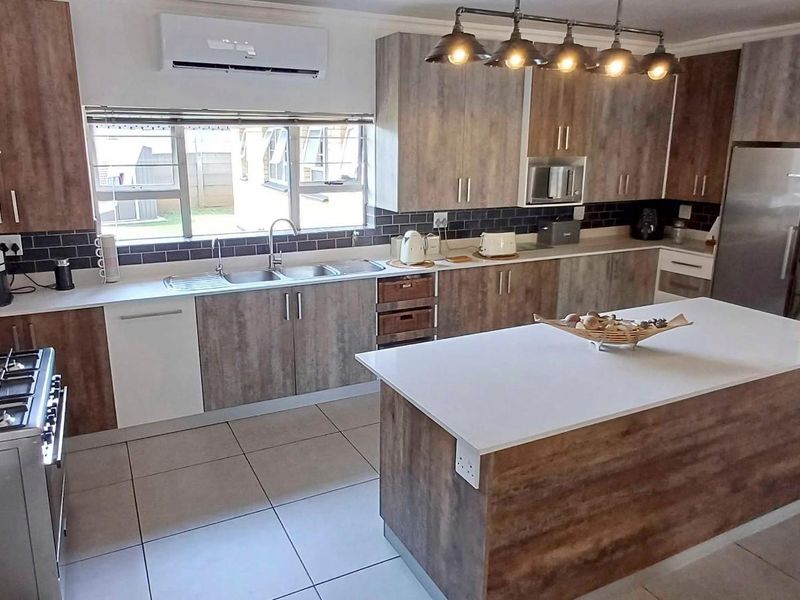 Modern kitchen featuring wood-look cabinetry, a central island with stone countertop, gas stove, subway tile backsplash, and tiled flooring.