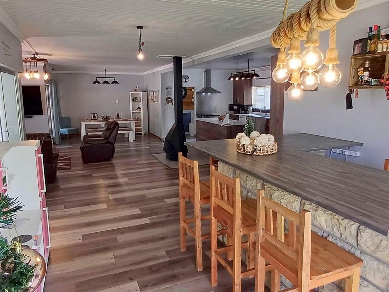 Spacious open-plan living area featuring wood-look flooring, a stone-clad breakfast bar, a central fireplace, and a modern kitchen with stainless steel extractor.