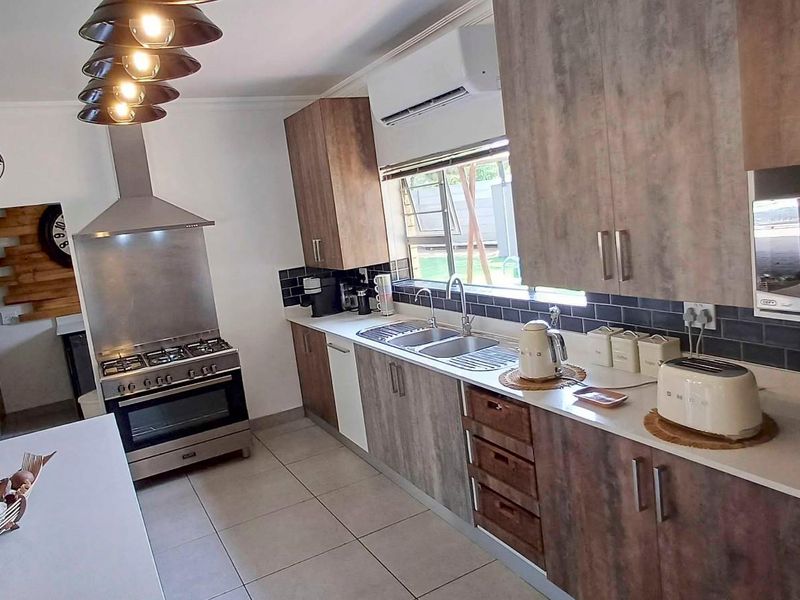 Modern kitchen featuring wood-look cabinetry, subway tile backsplash, stainless steel gas stove with extractor, built-in microwave, and tiled flooring.