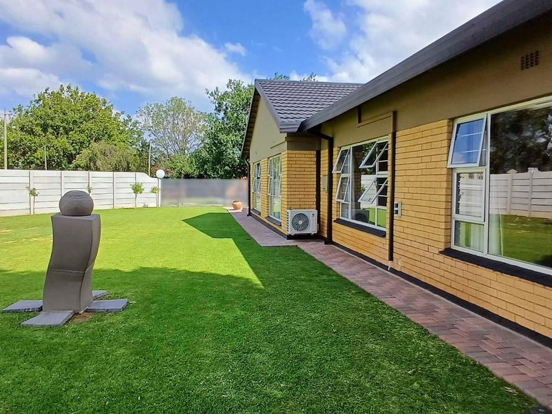 Rear view of the property featuring a well-maintained lawn, paved walkway, brick facade, and secure precast boundary walling.